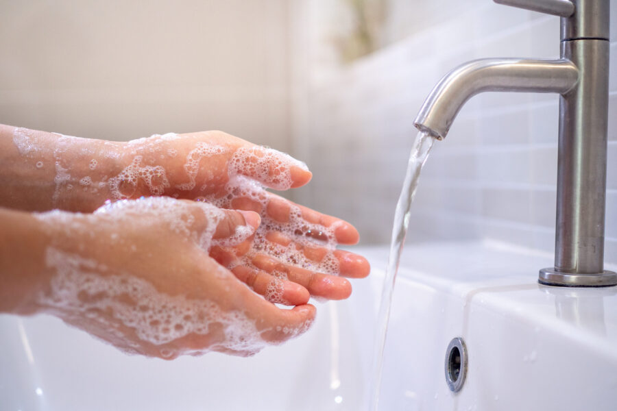 Close up of a person washing their hands with soap under running water at a sink.