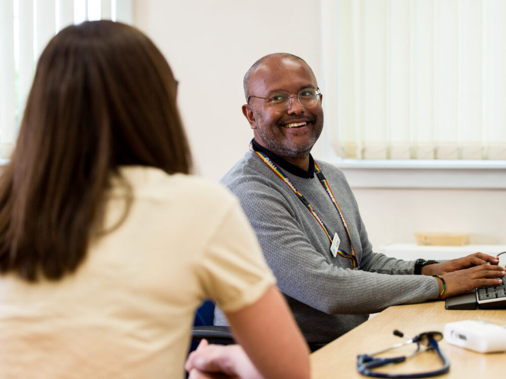 Male GP sitting at a desk speaking to a female patient