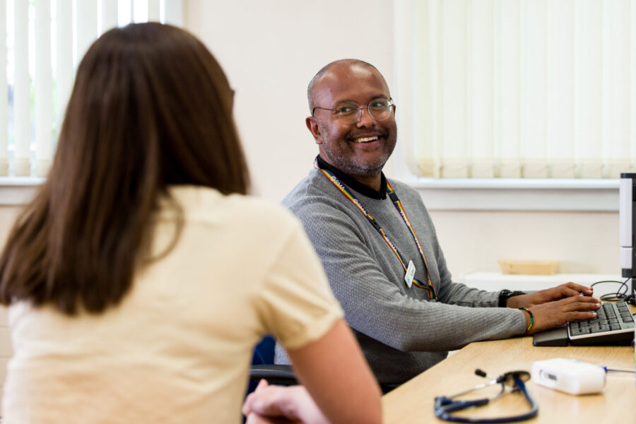 Male GP sitting at a desk speaking to a female patient