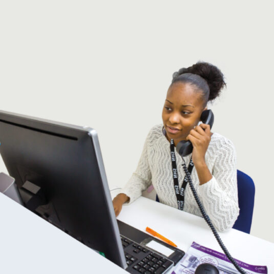 Healthcare worker speaking on the phone at a GP support or advice desk.