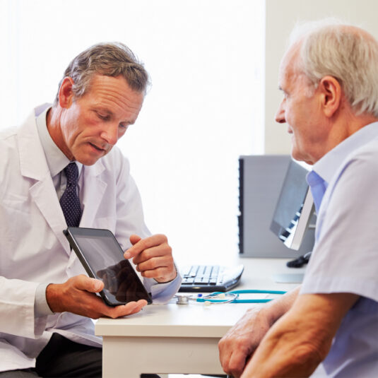 Doctor showing elderly male patient information on ipad