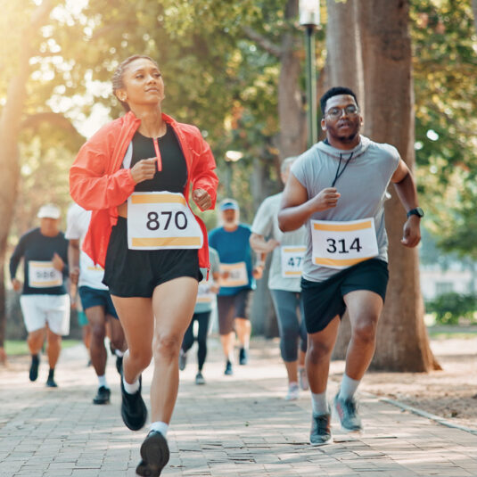 People taking part in a running race or charity fun run in a park, wearing numbered bibs.