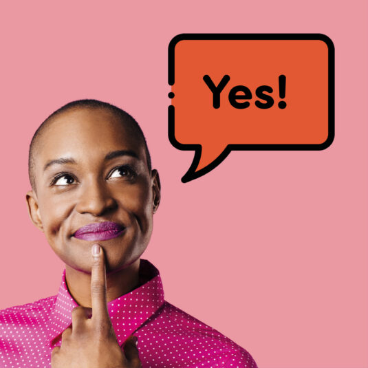 A woman smiling thoughtfully with a speech bubble saying “Yes!” against a pink background.