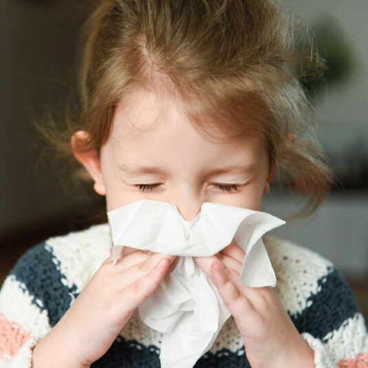 Child sneezing into a tissue with eyes closed