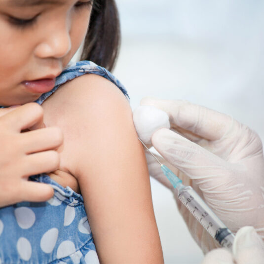 Healthcare worker giving a vaccine injection to a young child’s upper arm.
