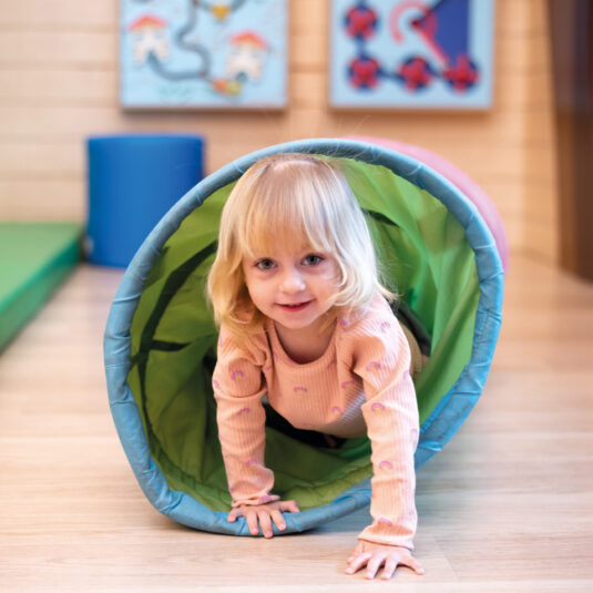 Young child crawling through a soft play tunnel in an indoor play area.