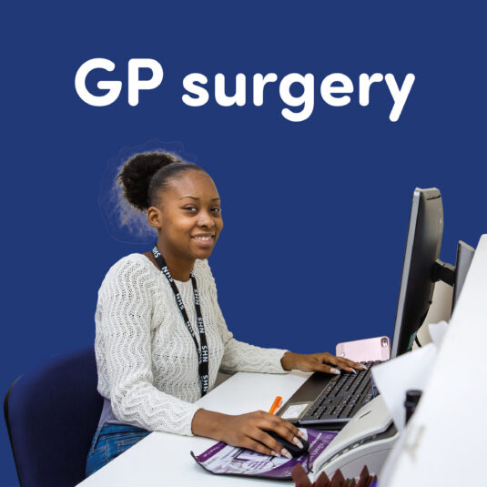Reception worker at a GP surgery sitting at a computer desk.