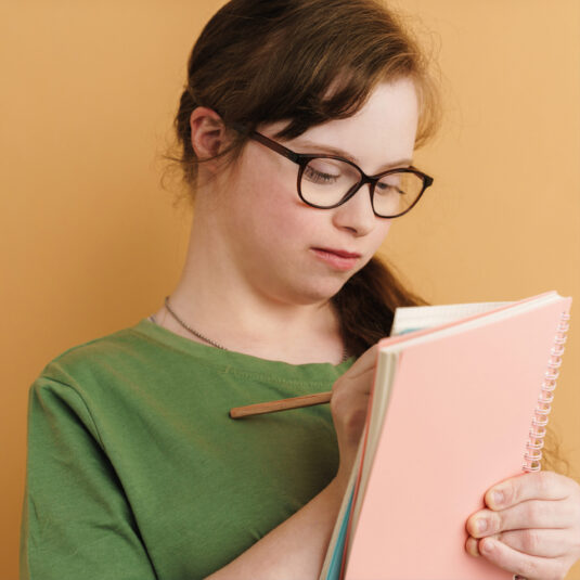Young girl wearing glasses writing notes in a notebook.