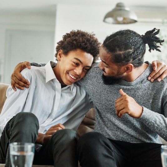 Adult and teenager sitting together on a sofa, sharing a supportive and affectionate moment.