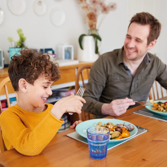 Parent and child smiling together while eating a meal at a dining table.