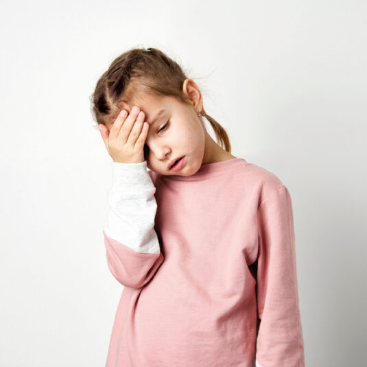 Young girl holding her head and looking unwell, suggesting symptoms such as headache, fever, or fatigue.