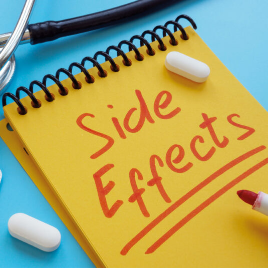 Notebook with the words “Side Effects” written on it, alongside pills and medical equipment, representing possible medication or vaccine side effects.