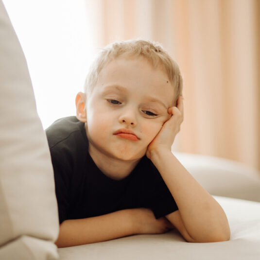 Young boy resting his head on his hand and looking tired or unwell.