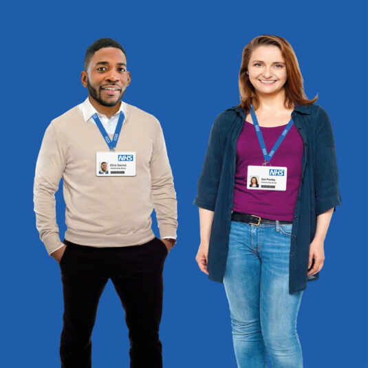 Two NHS workers wearing identification badges and standing against a blue background.