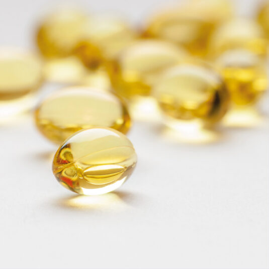 Close-up of yellow transparent supplement or vitamin capsules on a white surface.