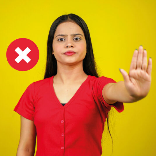 Woman holding up her hand in a “stop” gesture beside a red X symbol, indicating refusal, warning, or prevention.