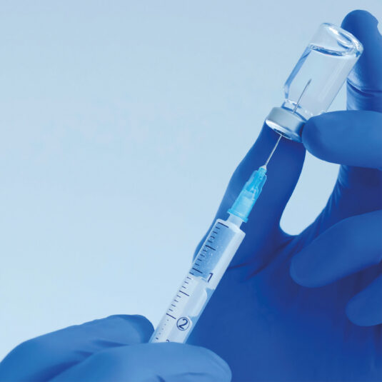 Close-up of gloved hands preparing a syringe and vaccine vial for injection.