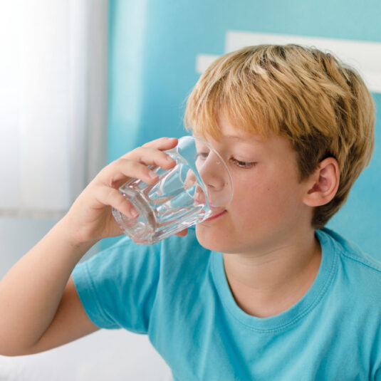 Young boy drinking a glass of water, representing hydration and healthy fluid intake during illness or recovery.