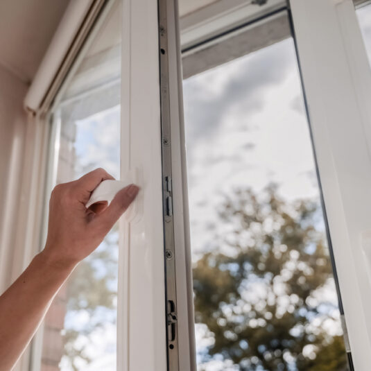 Hand opening a window, suggesting letting fresh air into a room for ventilation.