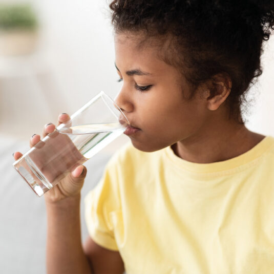 Young girl drinking a glass of water, showing the importance of staying hydrated during illness.