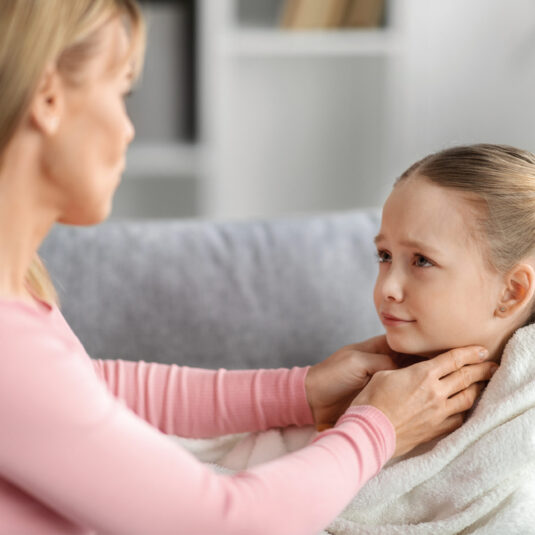 Mother gently checking a child’s neck/throat, indicating examination for swollen glands or sore throat symptoms.