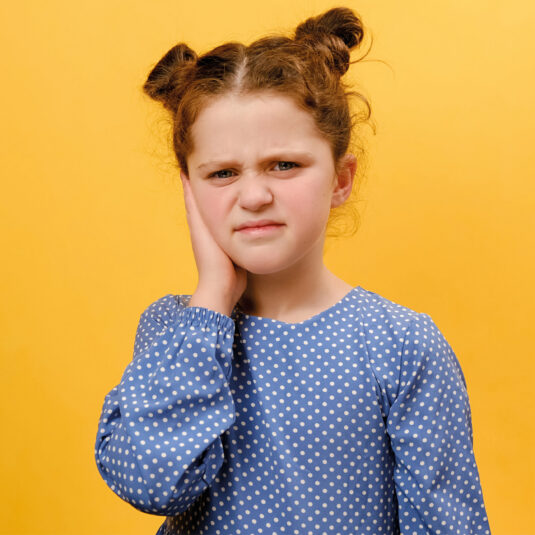 Young girl holding her ear with a pained expression, indicating earache or ear infection symptoms.
