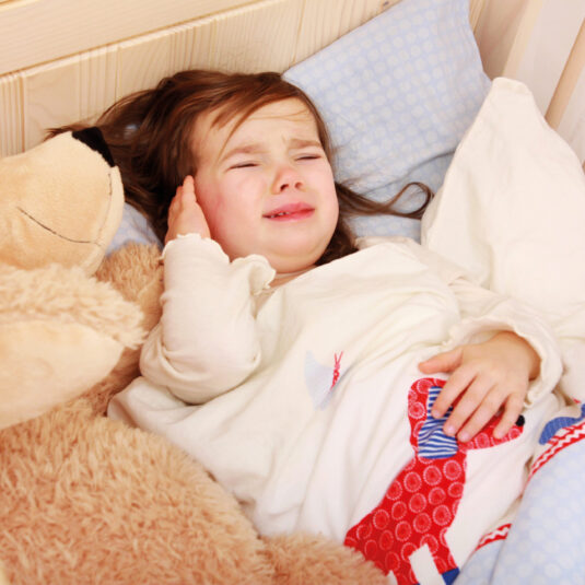 Young girl lying in bed holding her ear and crying, showing severe ear pain or discomfort from an ear infection.
