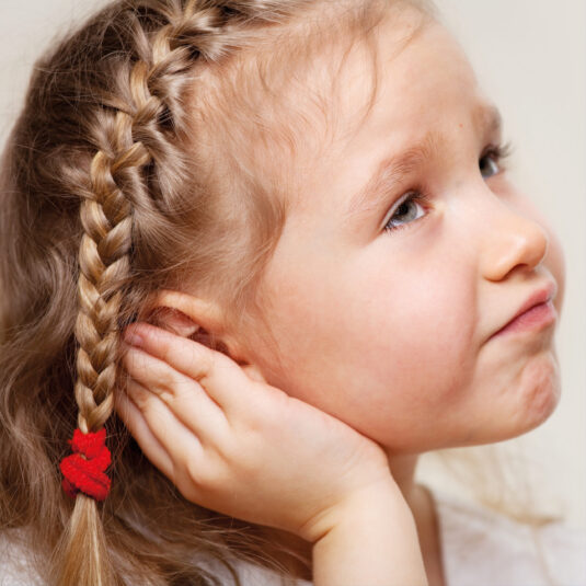 Young girl holding her ear with a concerned expression, suggesting earache or hearing discomfort.