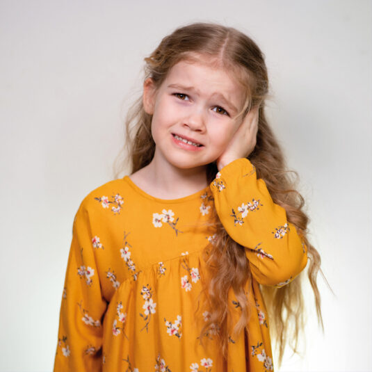 Young girl touching her ear with a worried expression, indicating persistent ear pain or possible ear infection symptoms.