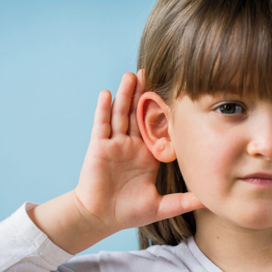 Young girl cupping her ear with her hand, suggesting hearing difficulty or reduced hearing after an ear infection.