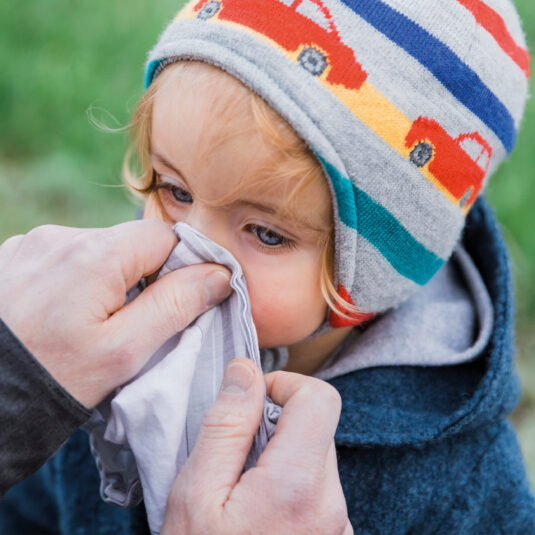 Small child having their nose wiped with a tissue, showing cold or upper respiratory infection symptoms linked to ear infections.
