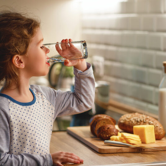 Young girl drinking a glass of water, representing the importance of staying hydrated during illness or recovery.