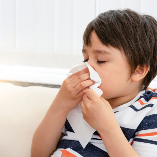 Child blowing their nose with a tissue, illustrating cold or congestion symptoms that may affect the ears.