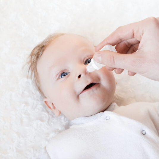 Baby receiving nasal saline drops, showing a method used to relieve nasal congestion in infants.