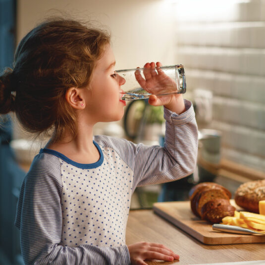 Young girl drinking water at a kitchen table, emphasizing fluid intake and hydration during recovery.