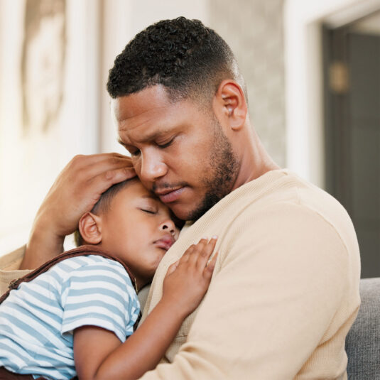 Father comforting a sleeping sick child, representing parental care and reassurance during illness.