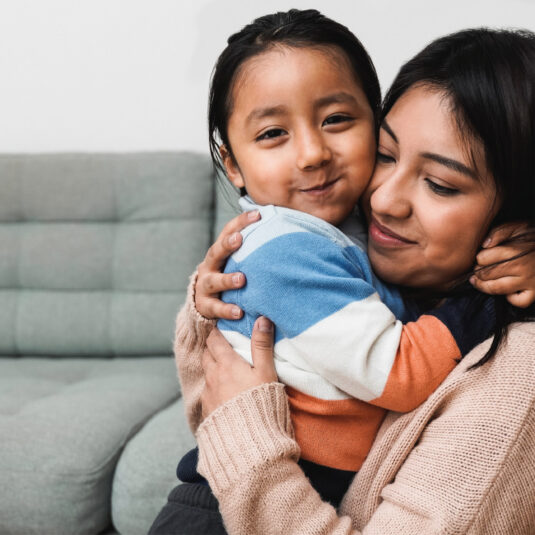 Mother hugging a smiling child, symbolising family support, comfort, and wellbeing.